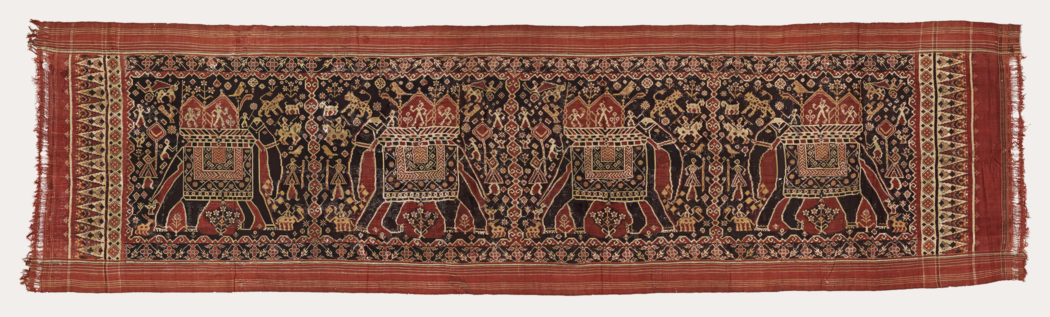Black, pale yellow and red rectangular cloth with white outlines. Four elongated elephants next to each other, separated by three vertical bands of intricate designs. A band of triangles repeat at the smaller ends.