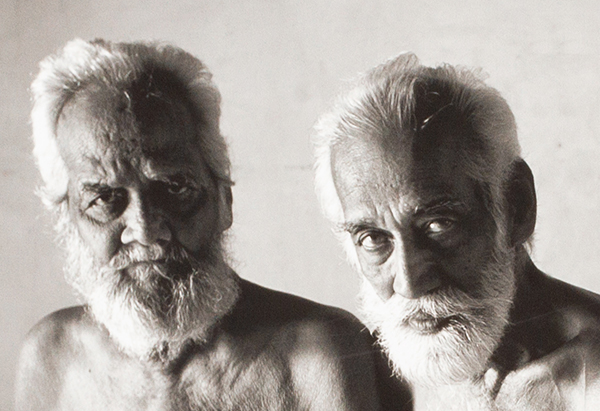 A detail of a photograph showing two elderly men with a stream of light falling on their faces attentively looking towards us.