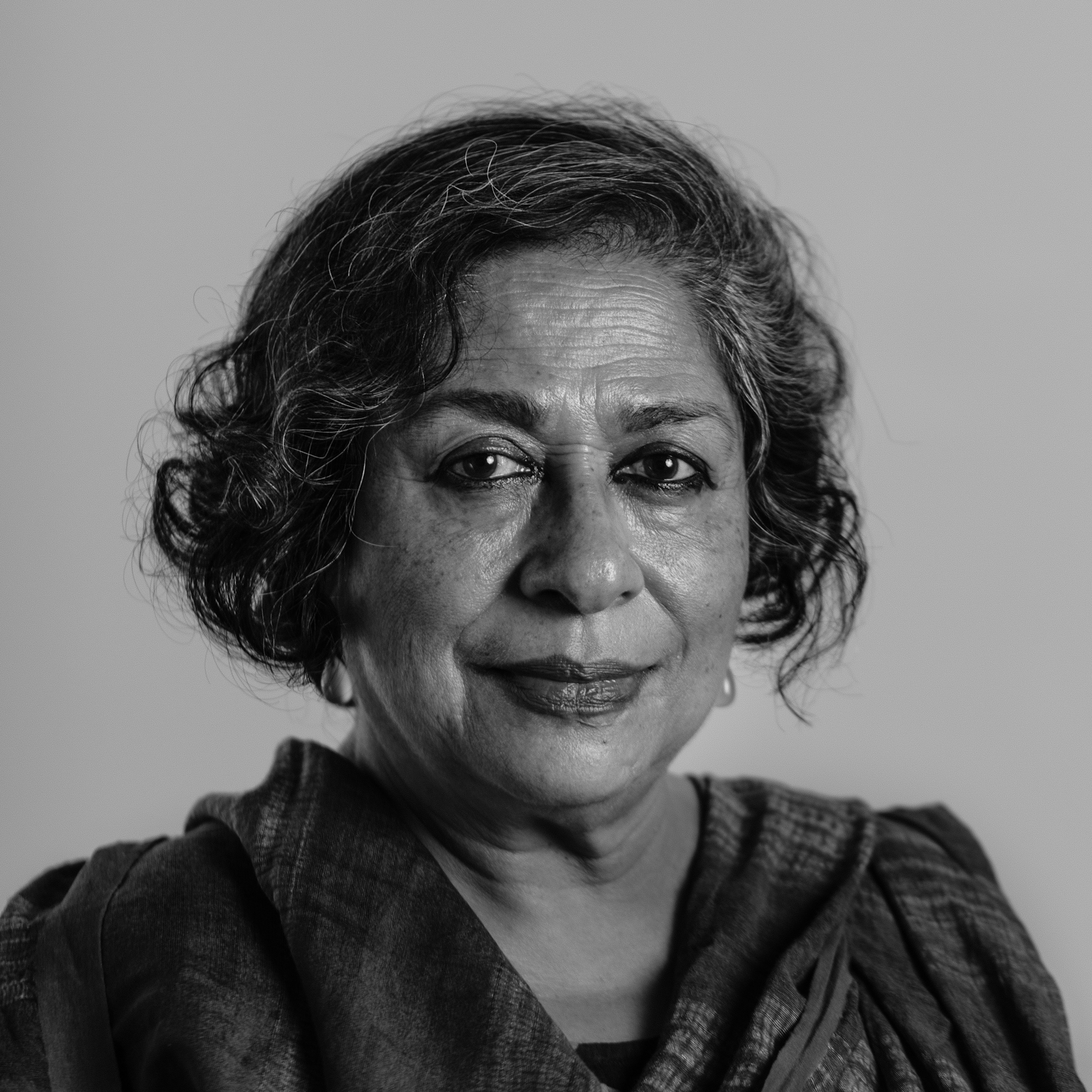 Arundhati Nag in black and white with graying, curling, chin length hair with a scarf around her shoulders.