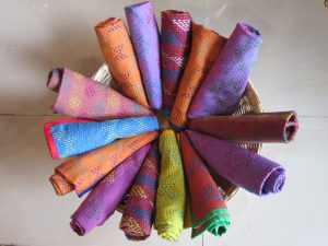 A cane basket of rolled embroidered textiles in orange, blue, red, pink and purple.