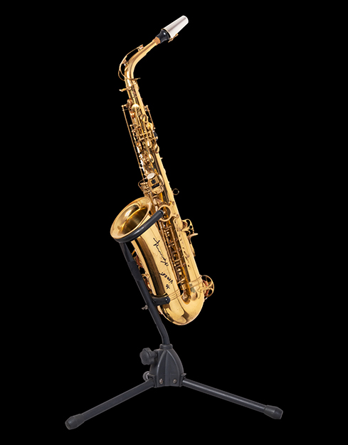 A gold metal saxophone placed on a stand with Kenny G’s autograph on the bell shaped body.