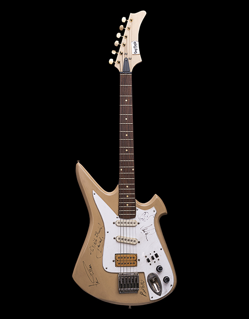 A sleek guitar with autographs of Deep Purple band members all over. Using a black marker, the band members have scribbled notes like thank you and a doodle of a tiny guitar at the base of the guitar.