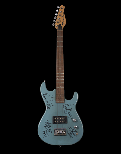 A guitar with a grey-blue body is covered with autographs of all the Rolling Stones band members scattered around. One of the scribbled autographs is Love, Mick Jagger. The head of the guitar has a Jansen logo.
