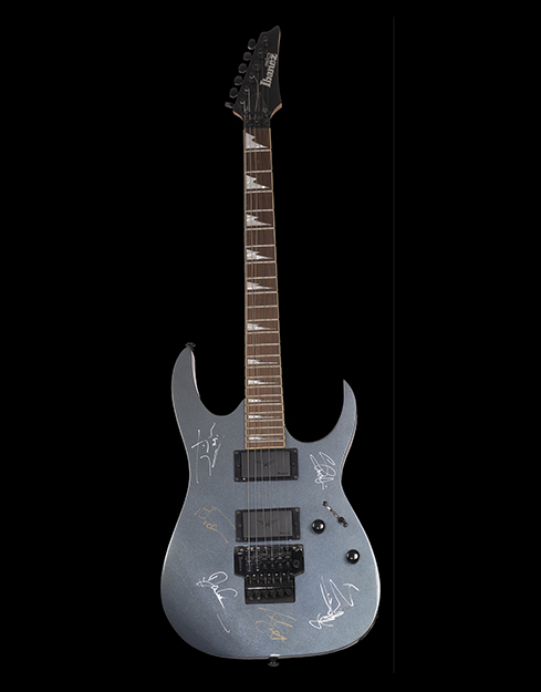 Slate grey textured guitar with an Ibanez logo at the center. Autographs of the band members are scattered everywhere at the base. The head of the guitar has Gio Ibanez written over it.