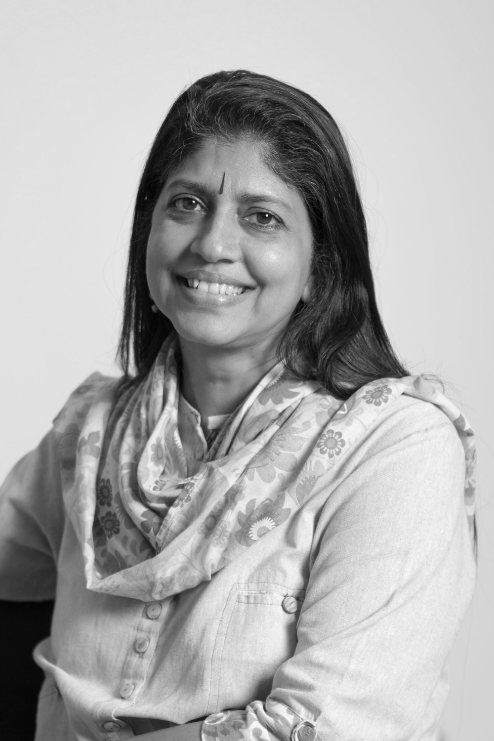Kamini Sawhney in black and white standing at an angle and smiling into the camera, she is wearing a bindi and dupatta across her shoulders.