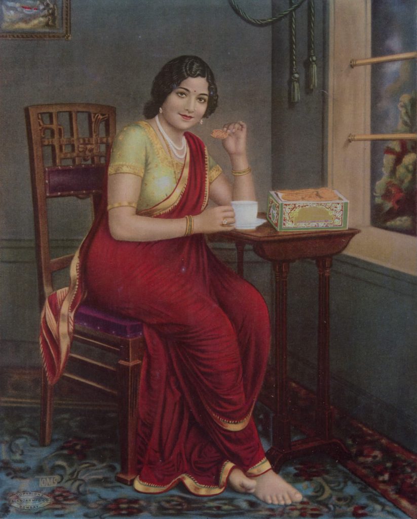 A woman seated on a chair smiles at us while holding a teacup on one hand and biscuit in the other.