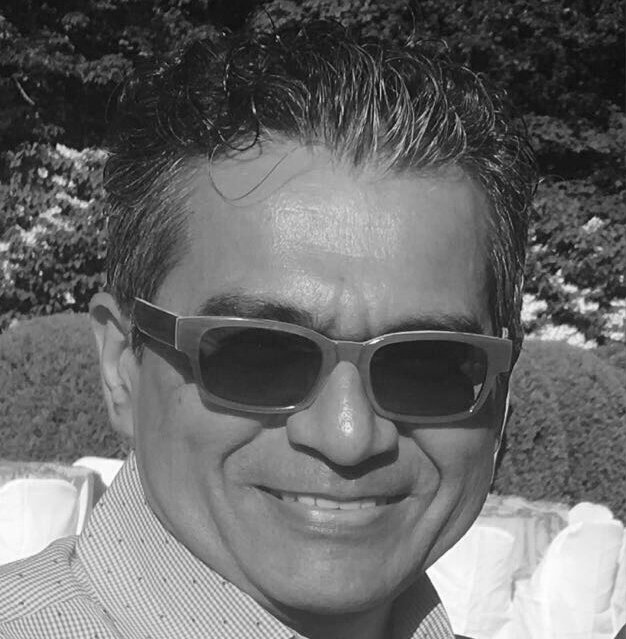 Rajiv Chaudhri in black and white wearing a printed collared shirt and sunglasses, smiling.