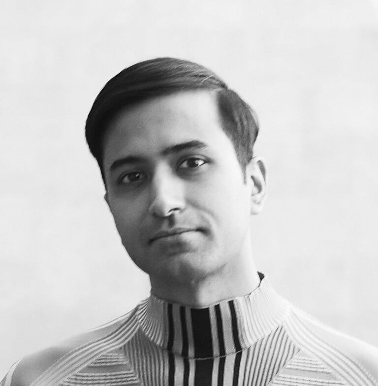 Shanay Jhaveri in black and white in a striped high necked shirt with his head slightly angled.