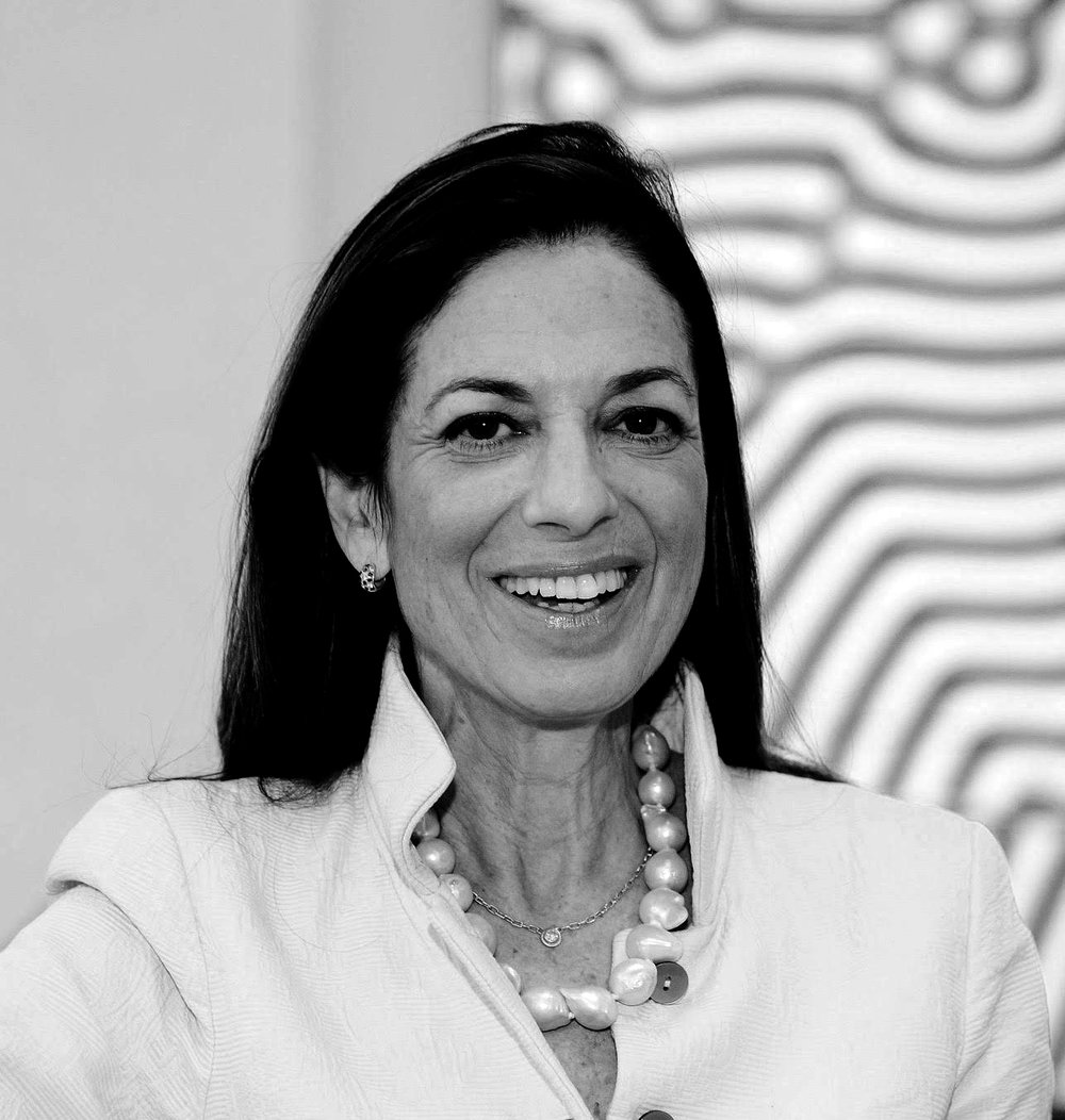 Susan Whitehead smiling in black and white in a white high collared shirt with a large beaded necklace.