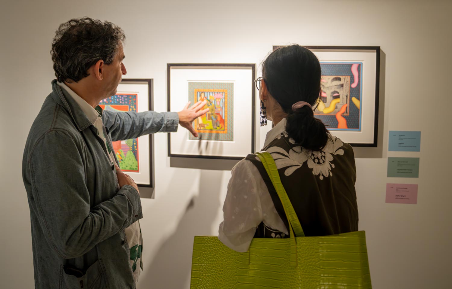 A person explains an artwork hung on a wall to an onlooker.