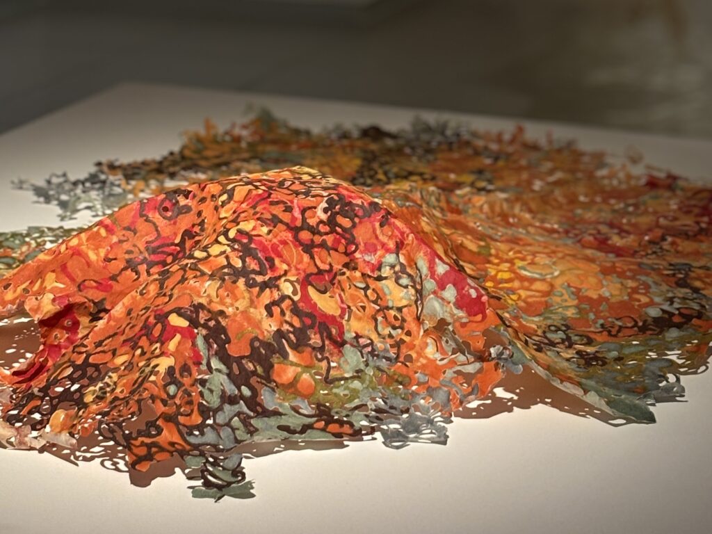 A delicate sculpture made of paper pulp of a vibrant orange, ochre, dark purple and muted grey colours