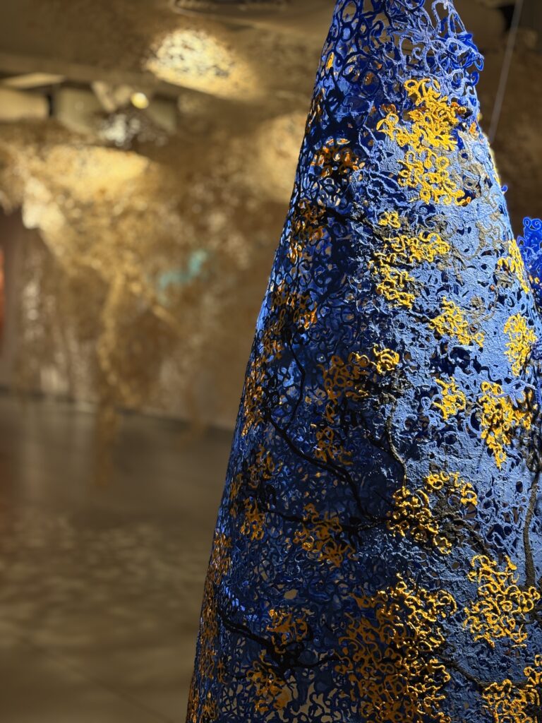 A close shot of one of the works of Ravikumar Kashi, a blue and yellow paper sculpture that hangs from the ceiling